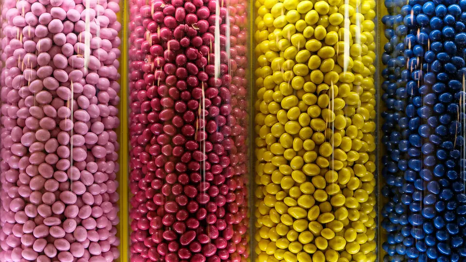 Glasbehållare med sockerpärlor i rosa, rött, gult och blått bredvid varandra